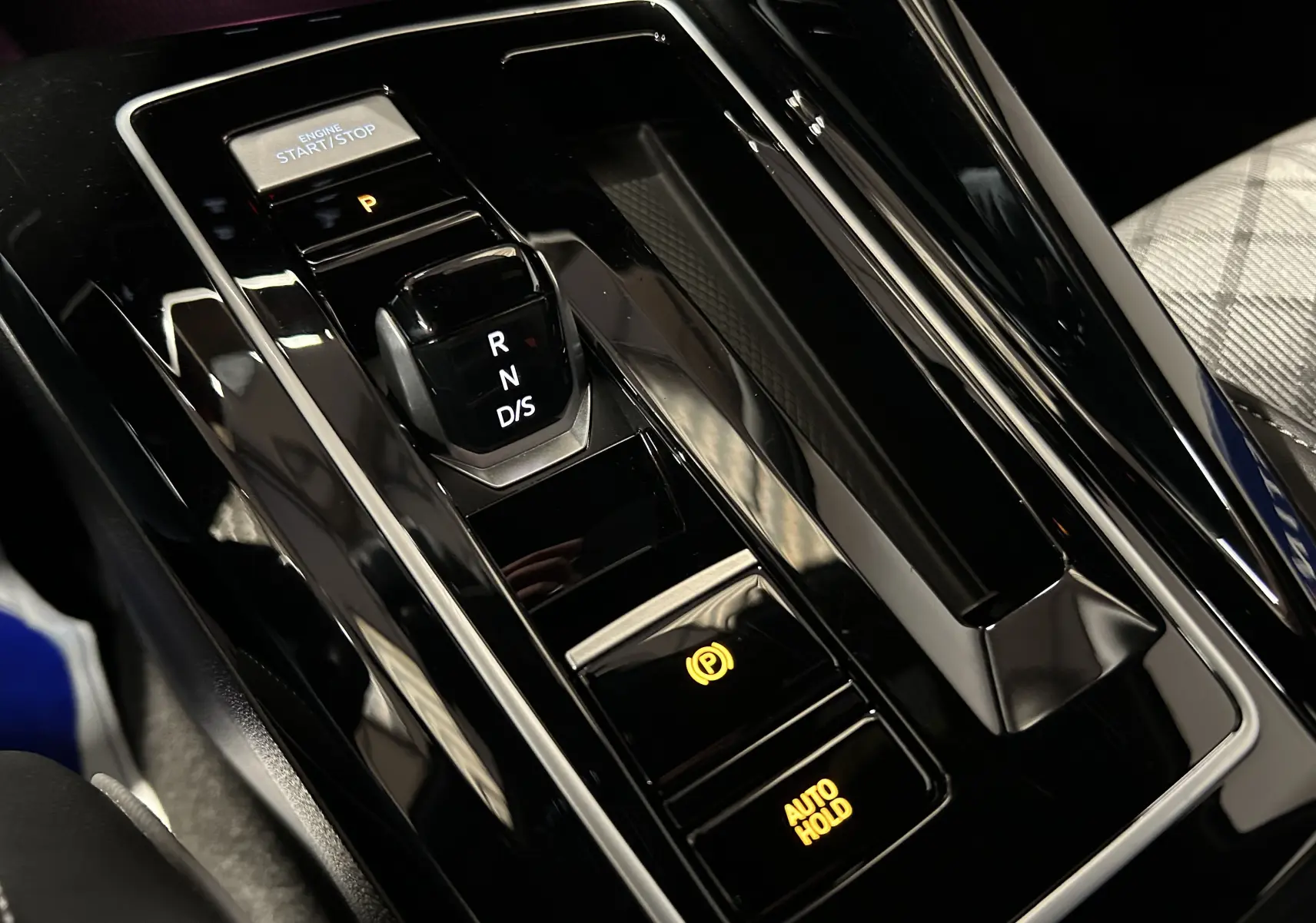 Gros plan sur la console centrale noire brillante de la Volkswagen Golf VIII eTSI avec levier de vitesse automatique et boutons éclairés.