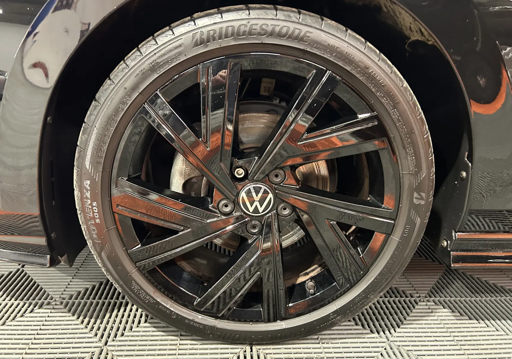 Gros plan sur la roue avant gauche noire métallisée d’une Volkswagen Golf VIII eTSI 150CH R-Line avec jante noire brillante.