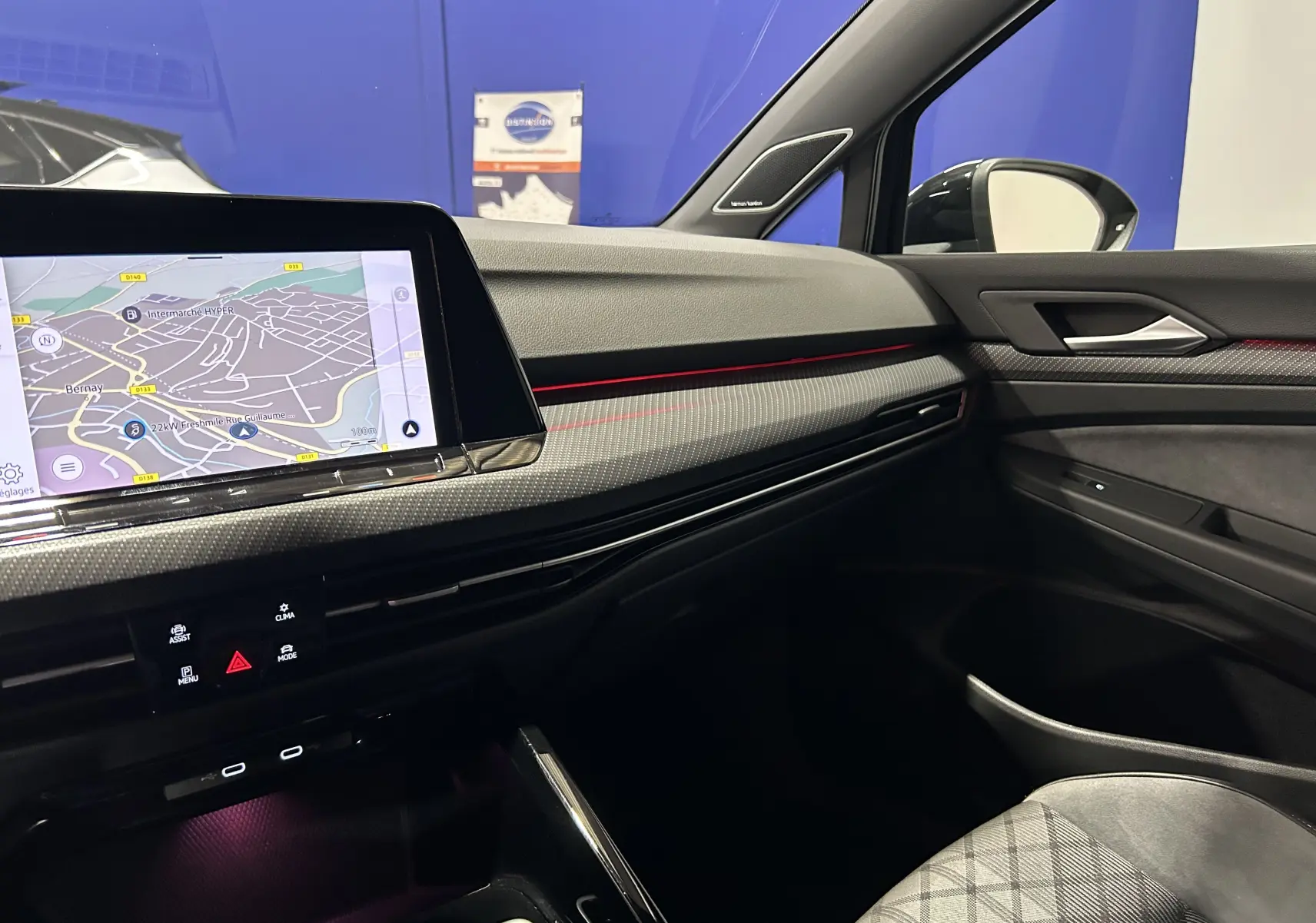 Vue intérieure côté passager de la Volkswagen Golf VIII eTSI noire, avec écran GPS et bandeau lumineux rouge sur la planche de bord.