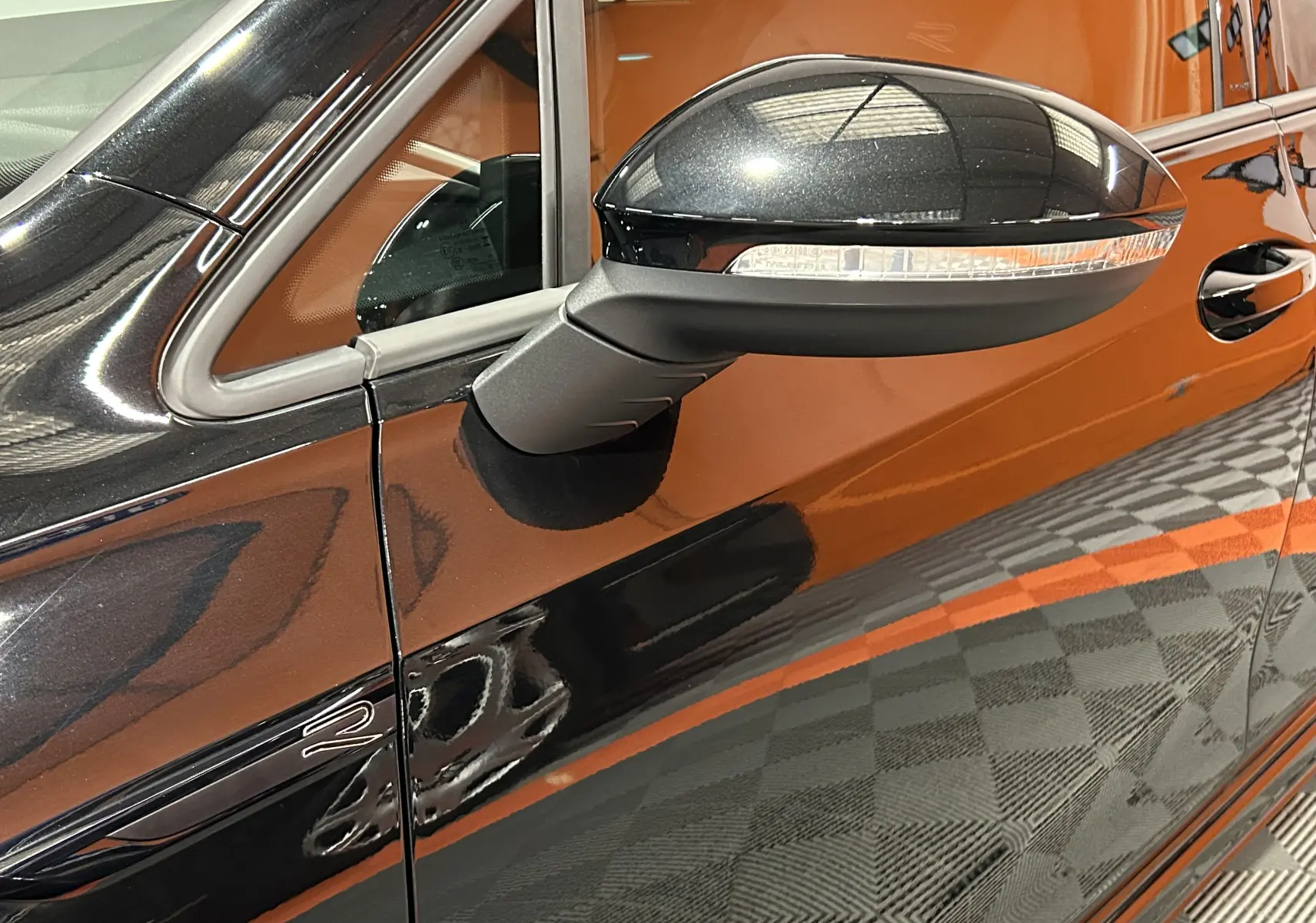 Gros plan sur le rétroviseur côté gauche d'une Volkswagen Golf VIII eTSI noir métal, reflet du capot et porte visible.