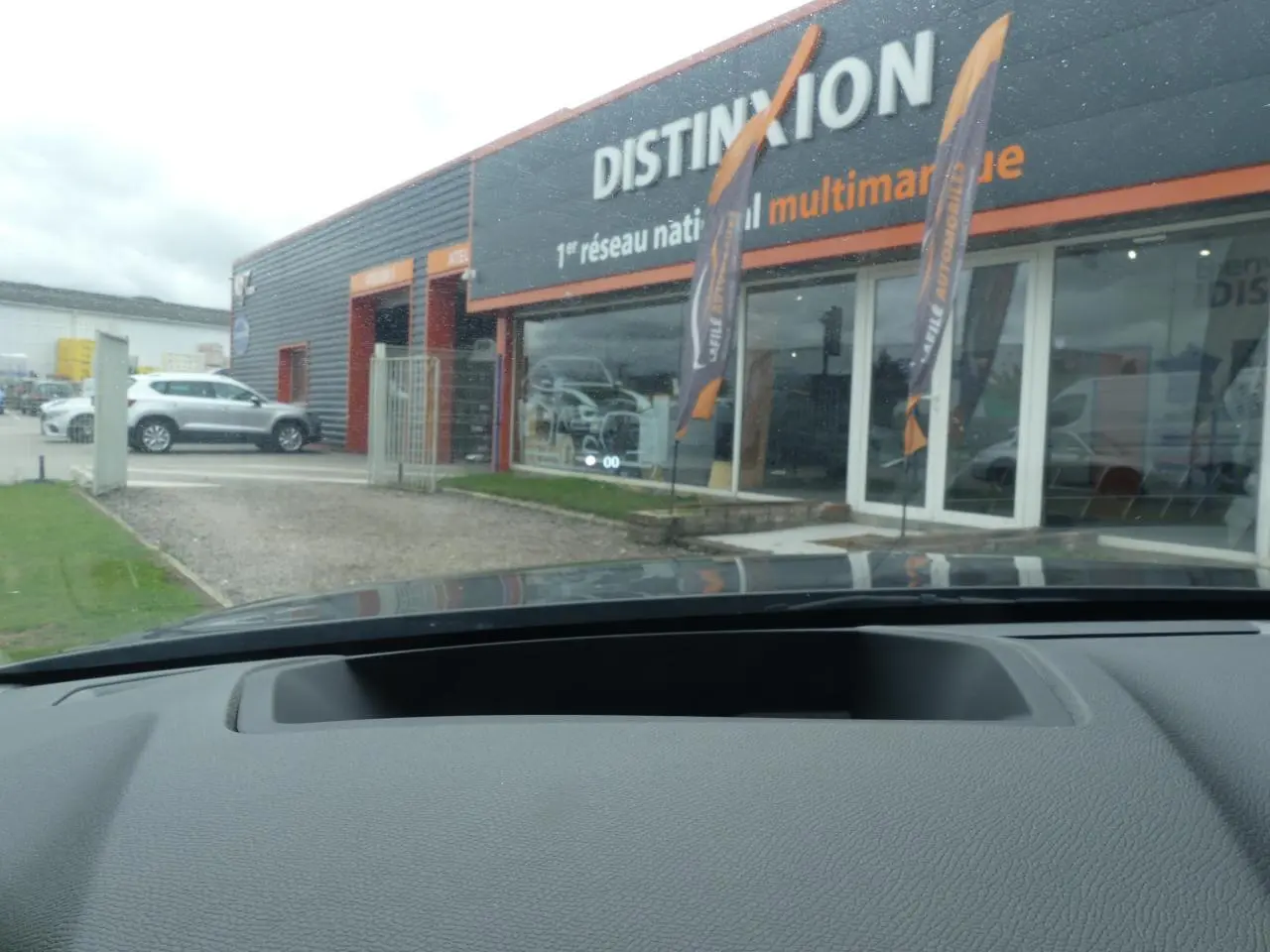 Vue depuis l'intérieur du DS4 2024 gris métallisé, montrant le tableau de bord et la vitrine du concessionnaire Distinxion.