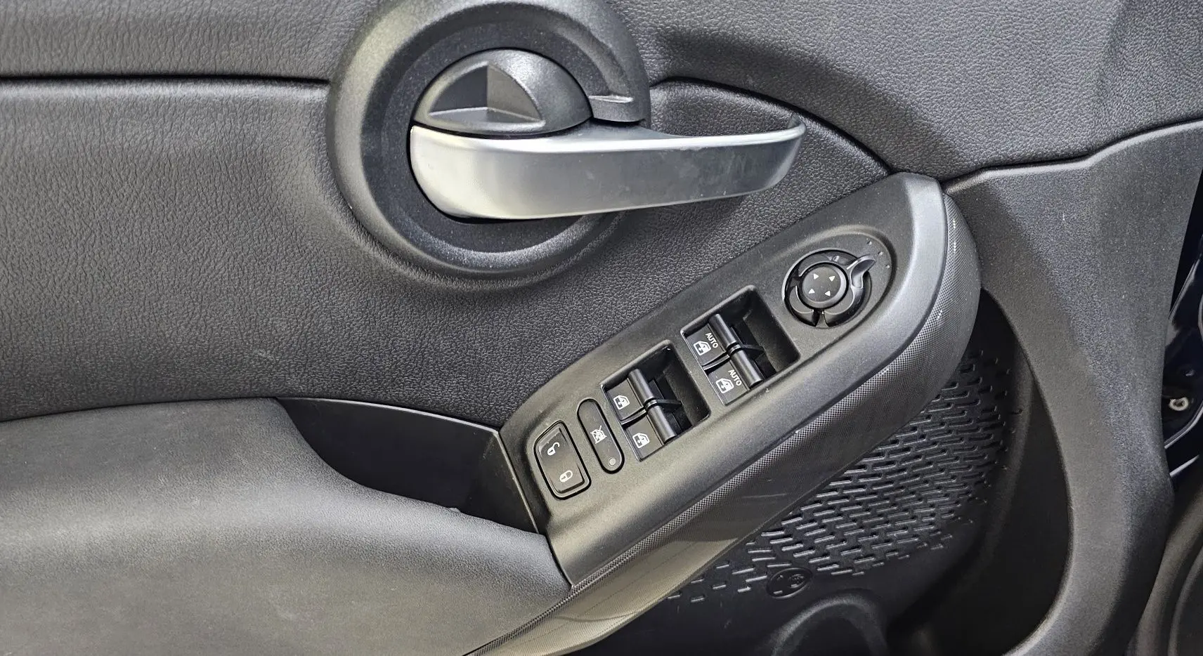 Gros plan sur la poignée intérieure et les commandes des vitres côté gauche d'une FIAT 500X Ph2 bleu 2024 hybride.