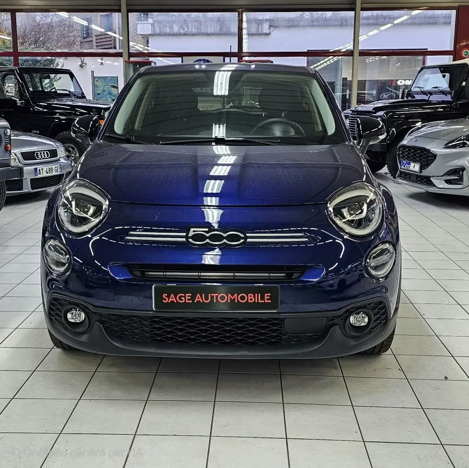 Vue frontale d'une FIAT 500X 2024 bleu profond avec logo 500 centré et phares ronds distinctifs dans un showroom.