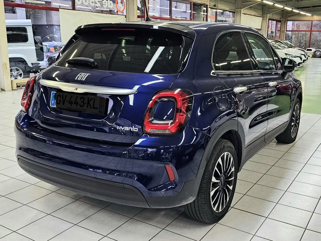 Vue 3/4 arrière droite d'un FIAT 500X bleu hybride 2024 avec feux arrière distinctifs et jantes alliage bicolores.