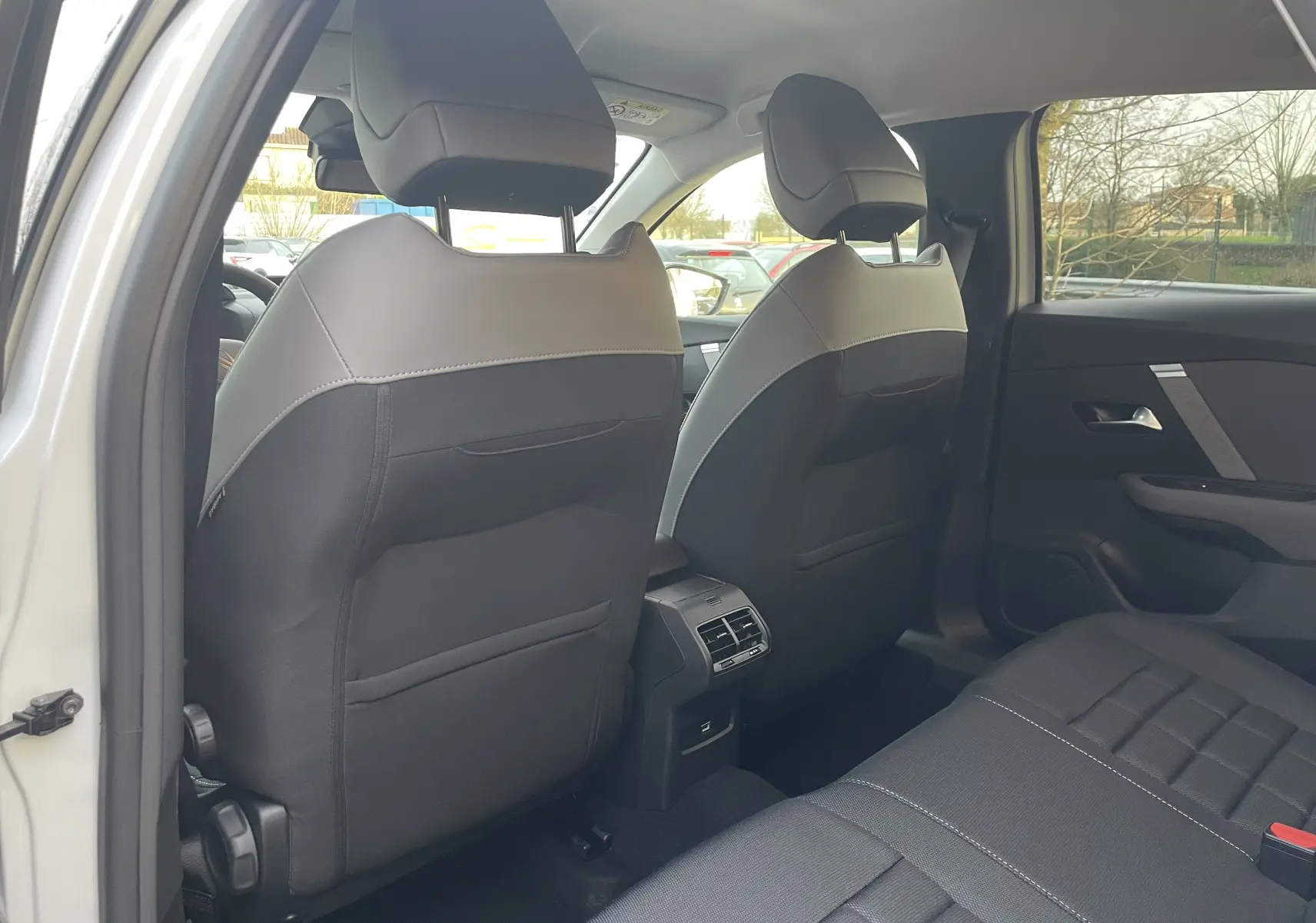 Vue intérieure arrière côté gauche montrant les sièges avant en tissu noir avec surpiqûres et les aérateurs centraux du Citroën C4 blanc.