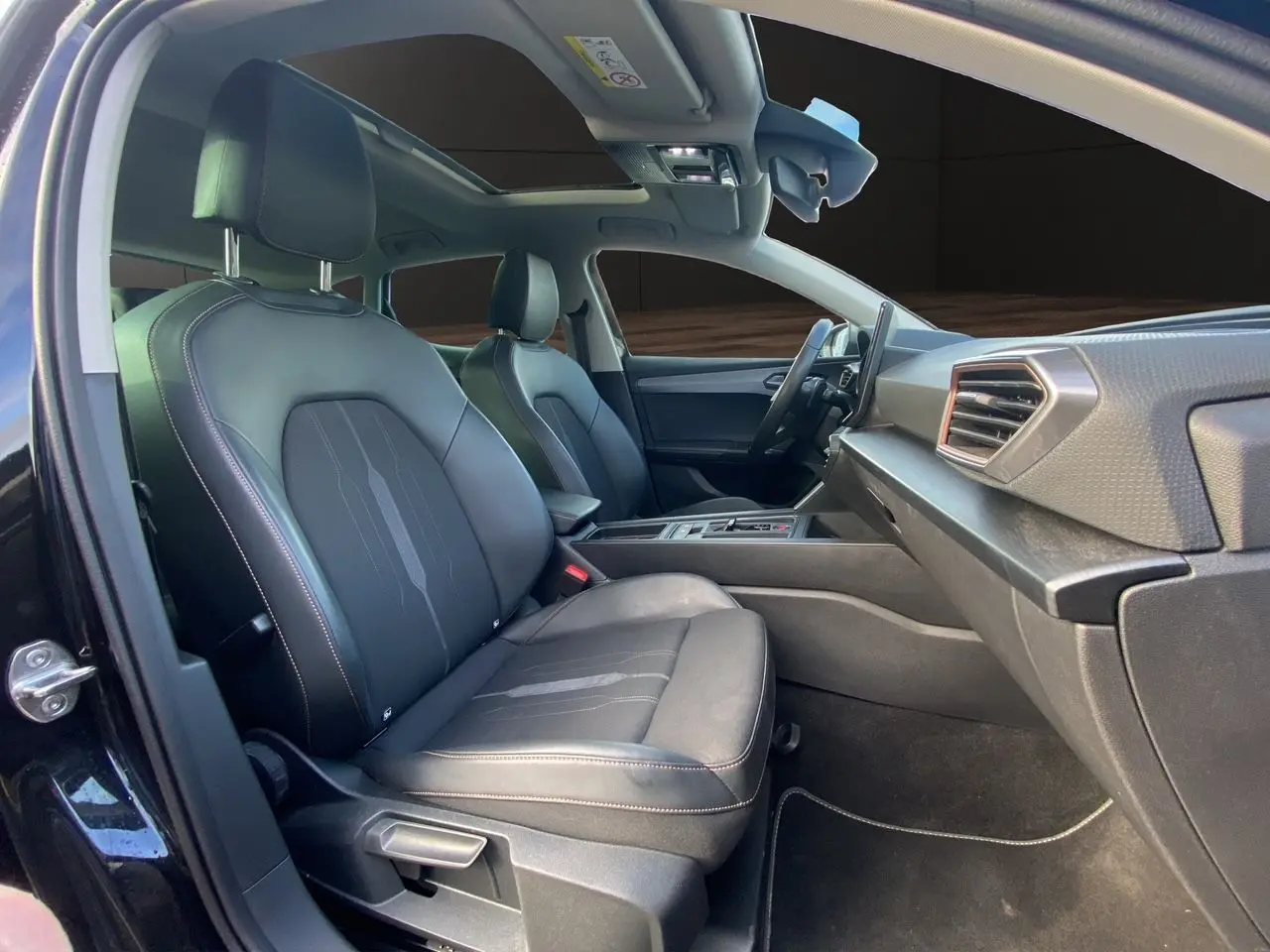 Intérieur noir de la CUPRA Leon 2023 vu côté passager, avec toit ouvrant panoramique et sièges en cuir tissu.