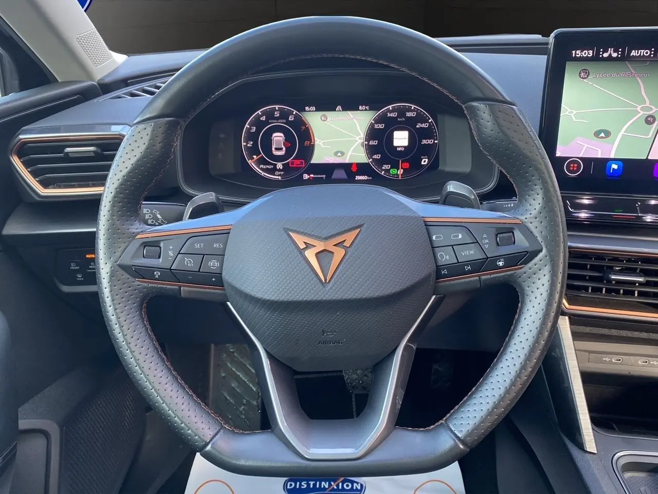 Vue rapprochée du volant noir perforé de la CUPRA Leon 2023 avec tableau de bord numérique et écran tactile de navigation.