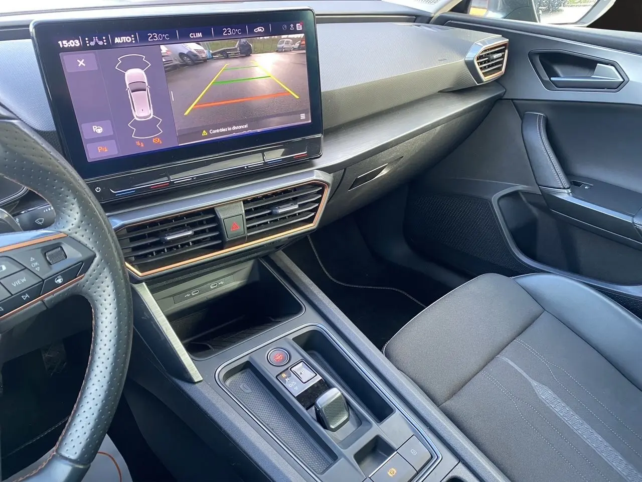 Vue intérieure côté passager de la CUPRA Leon noire 2023, avec écran tactile affichant la caméra de recul et volant perforé.
