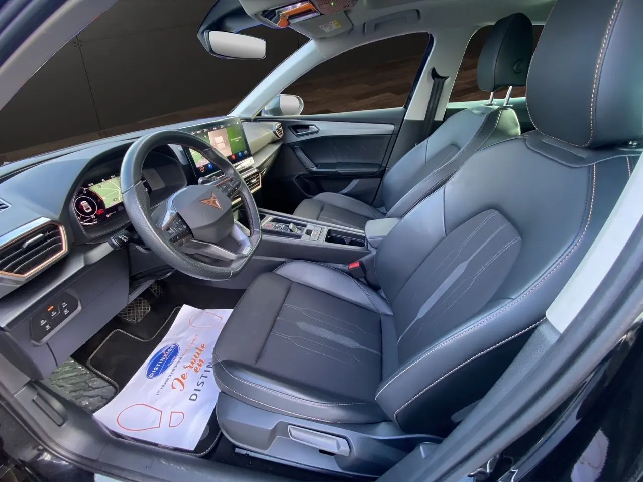 Vue intérieure côté conducteur de la CUPRA Leon 2023 noire, avec sièges cuir noir et tableau de bord digital.