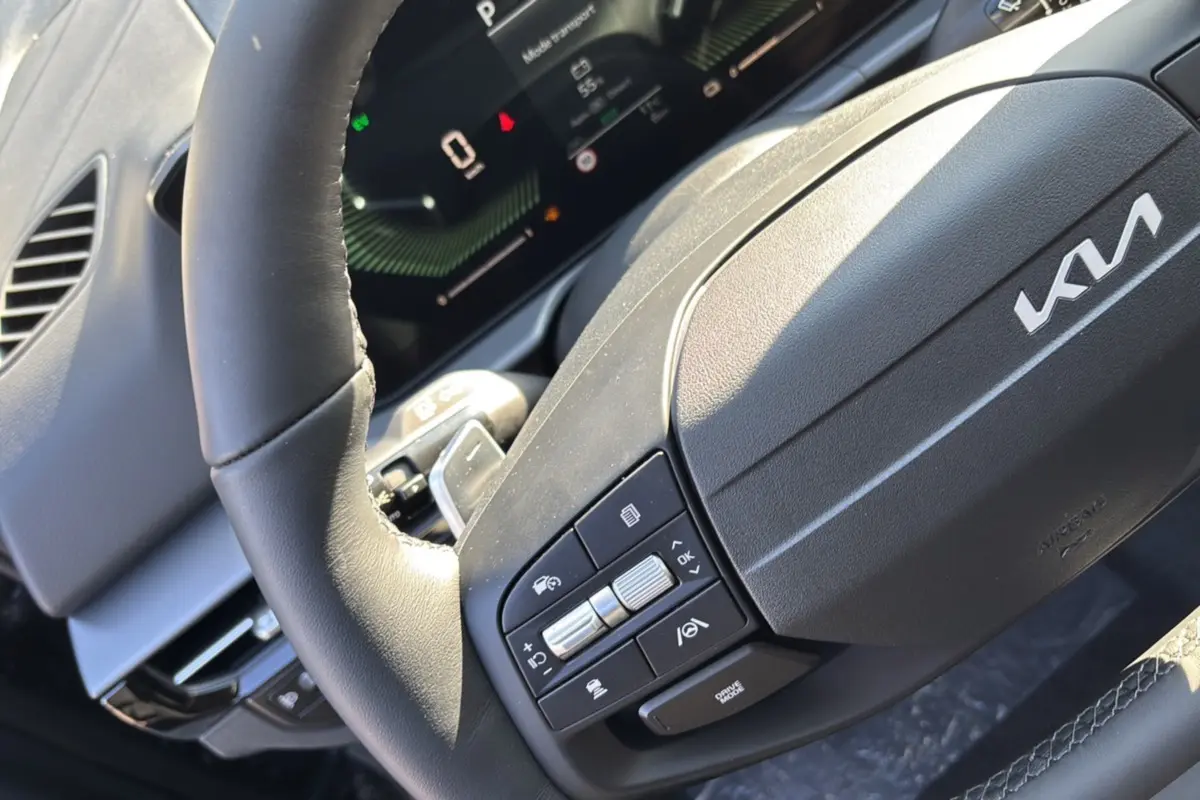 Gros plan sur le volant cuir multifonctions du Kia Sportage gris eclipse, avec commandes intégrées et tableau de bord numérique.