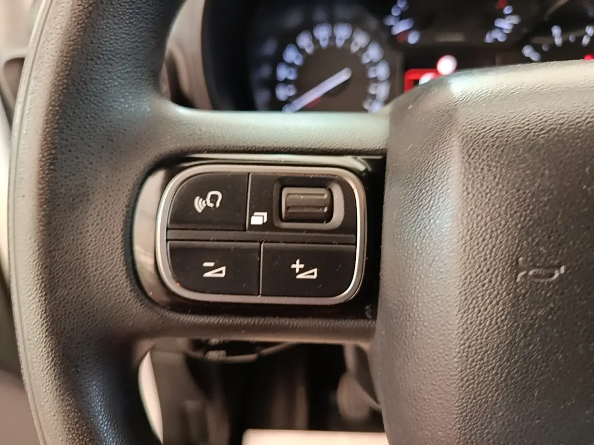 Gros plan sur les commandes multifonctions noires du volant de la Citroën Berlingo blanc, avec tableau de bord flou en arrière-plan.