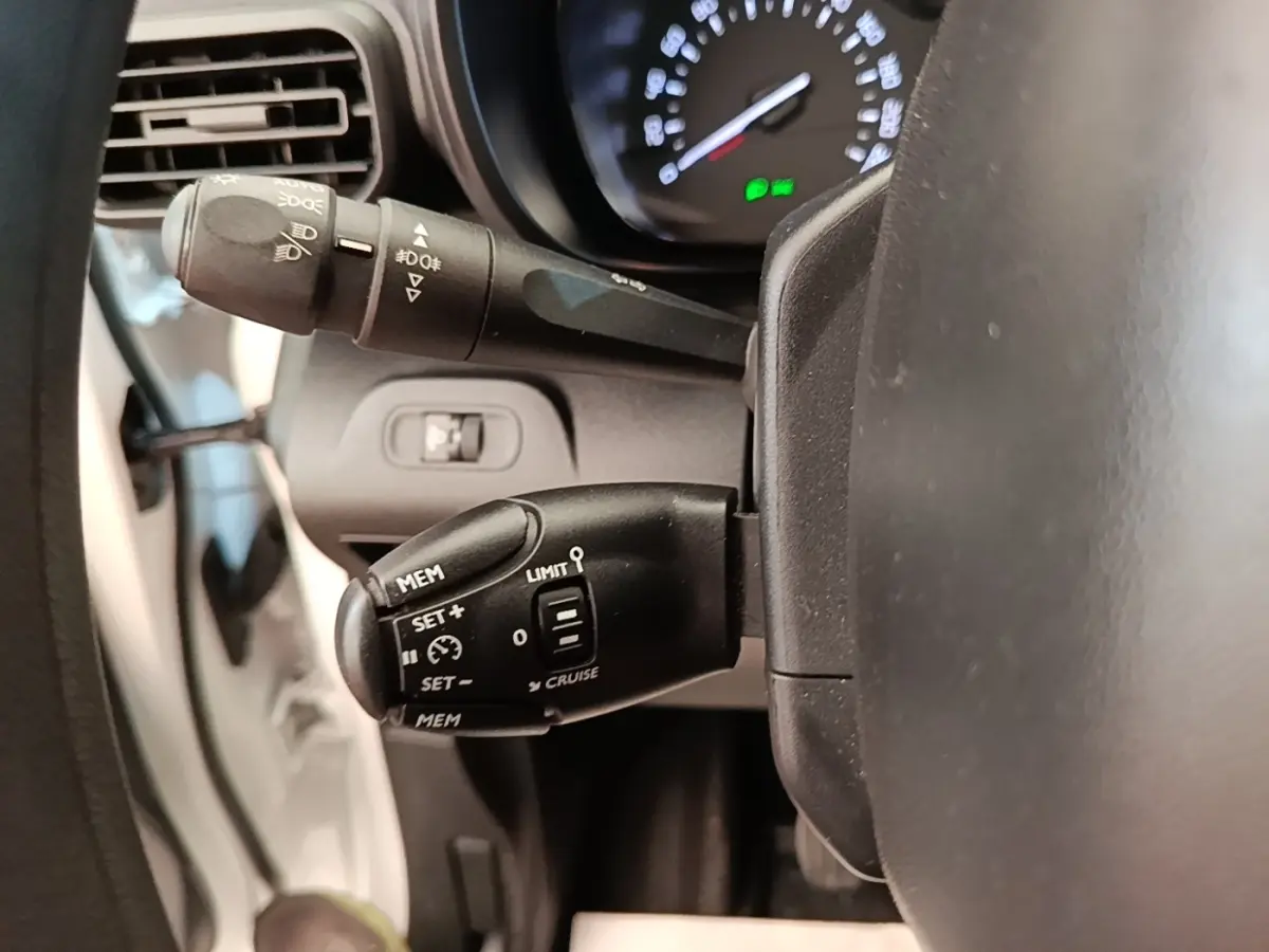 Gros plan sur le volant et commandes de régulateur de vitesse du Citroën Berlingo blanc, tableau de bord en arrière-plan.