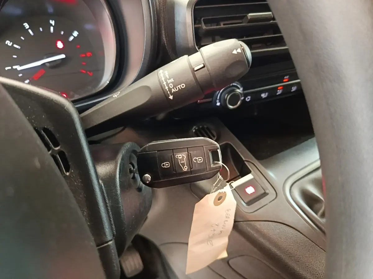 Gros plan intérieur sur le volant et le tableau de bord du Citroën Berlingo blanc avec clé insérée et commandes visibles.