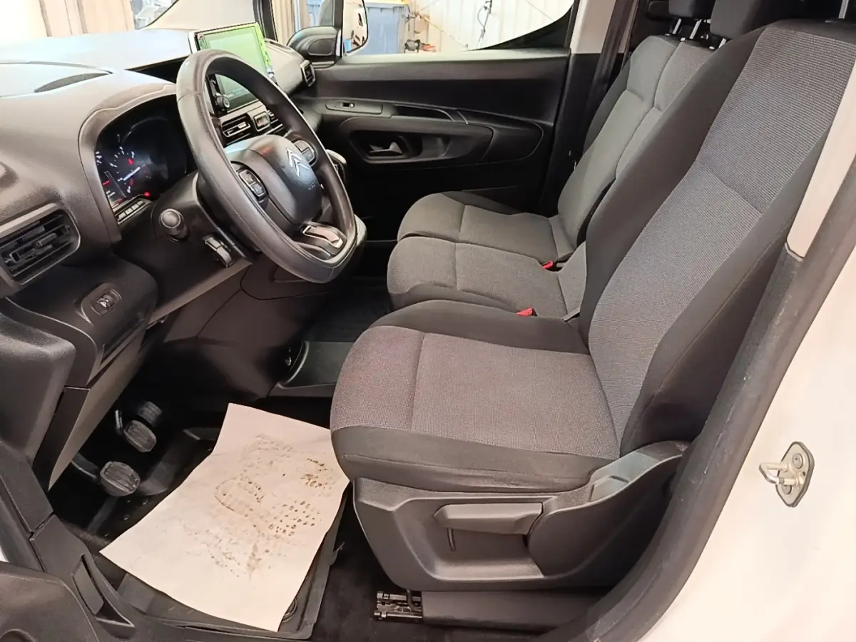 Vue intérieure côté conducteur du Citroën Berlingo blanc 2021, montrant le volant multifonctions et les sièges gris.