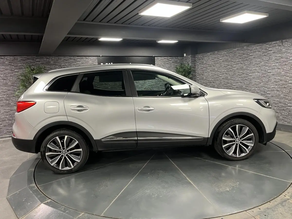 Profil côté gauche d'un Renault Kadjar gris platine 2017 avec jantes alliage 19 pouces dans un showroom.