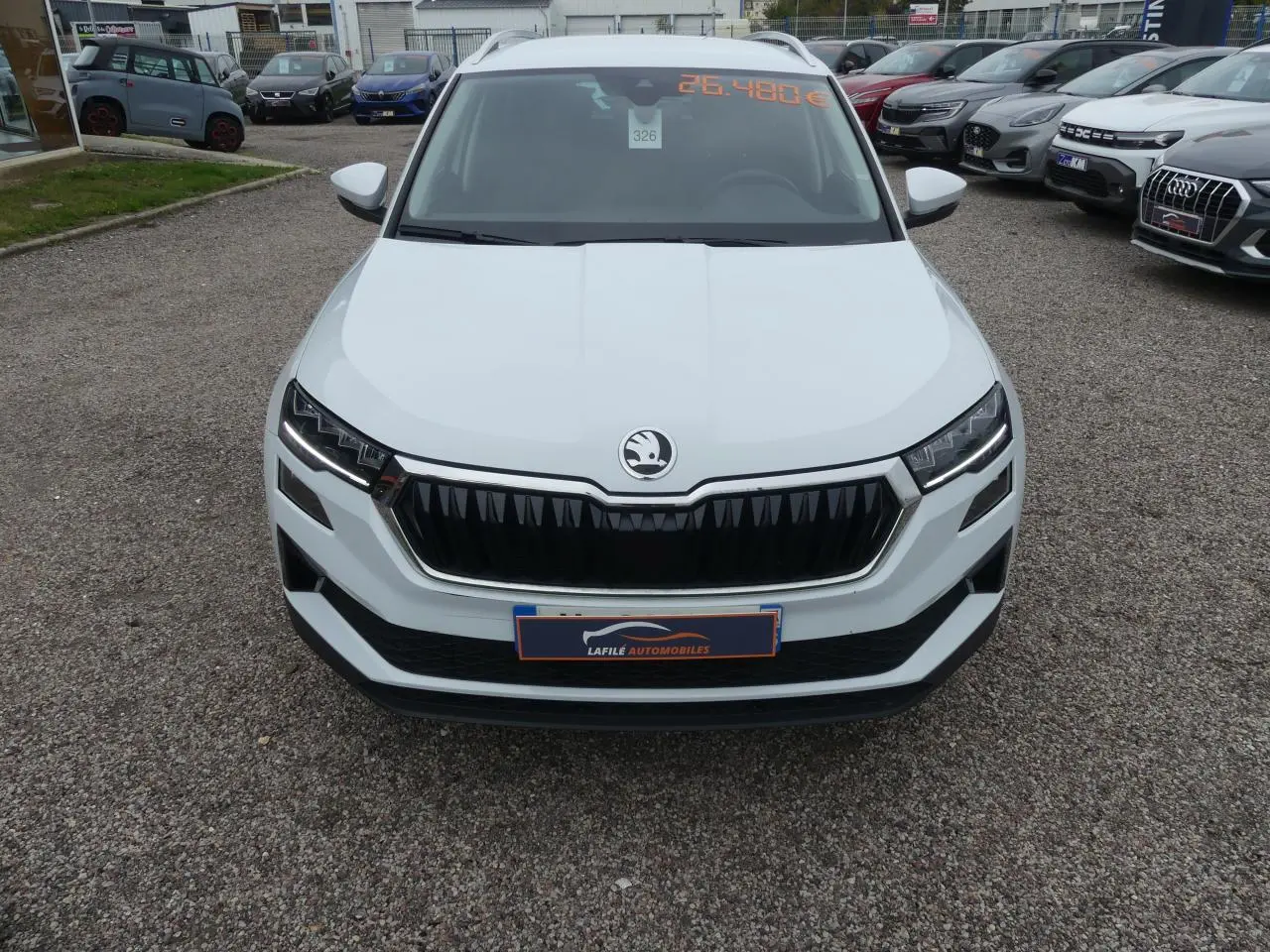 Vue avant d'un SUV Skoda Karoq blanc 2024 avec calandre noire et phares LED, en extérieur sur parking.