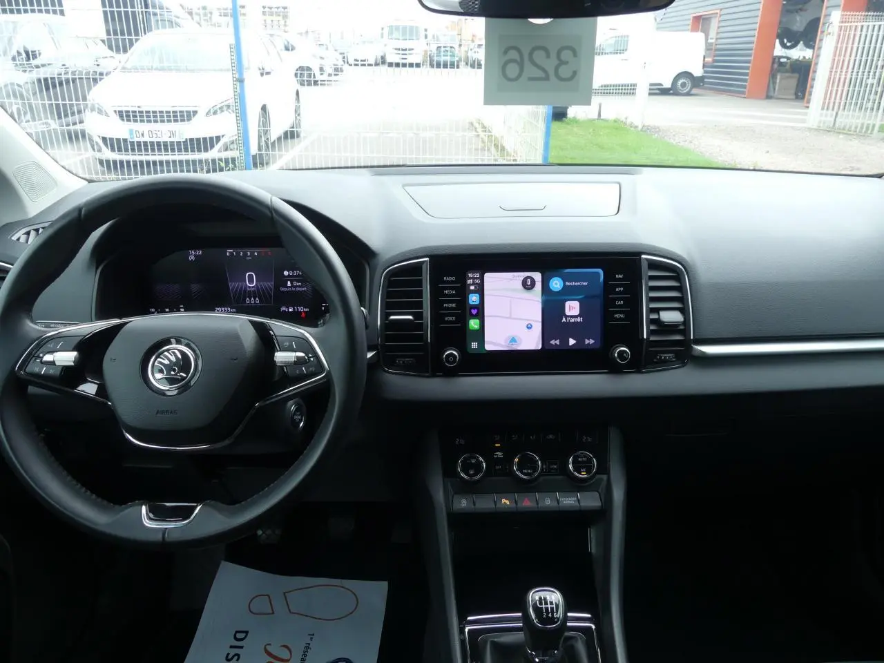 Vue intérieure frontale du tableau de bord du Skoda Karoq blanc 2024 avec écran tactile et volant multifonctions noir.