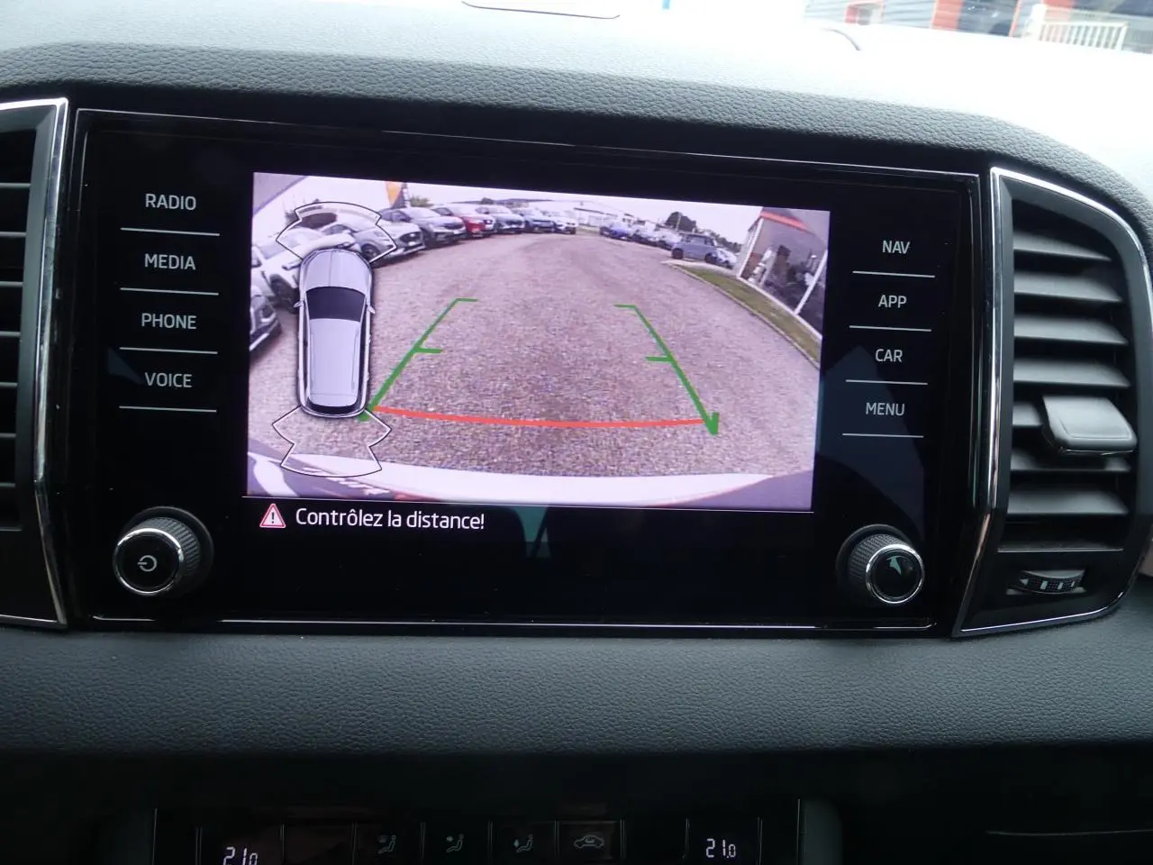 Écran tactile du tableau de bord montrant la caméra de recul avec vue arrière et alertes de distance du Skoda Karoq blanc.