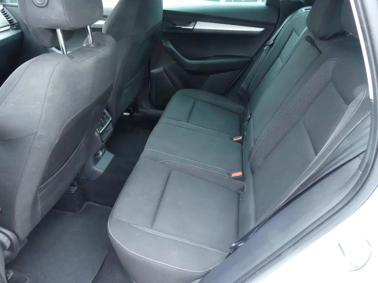 Vue intérieure côté droit de la banquette arrière noire tissu du Skoda Karoq blanc 2024 avec appuie-têtes et aérateurs centraux.