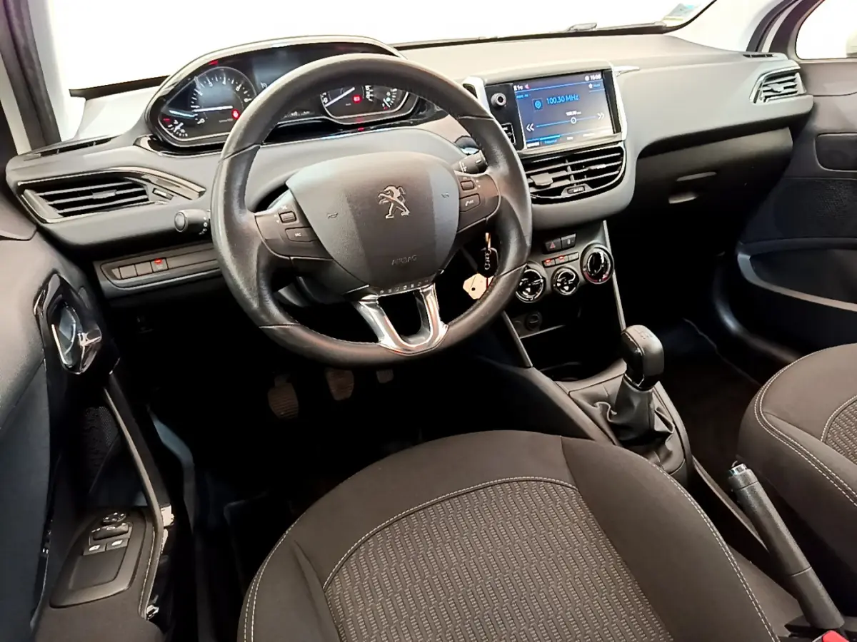 Intérieur noir de la Peugeot 208 Puretech 82 Signature 2019, vue du poste de conduite avec volant cuir et écran tactile central.