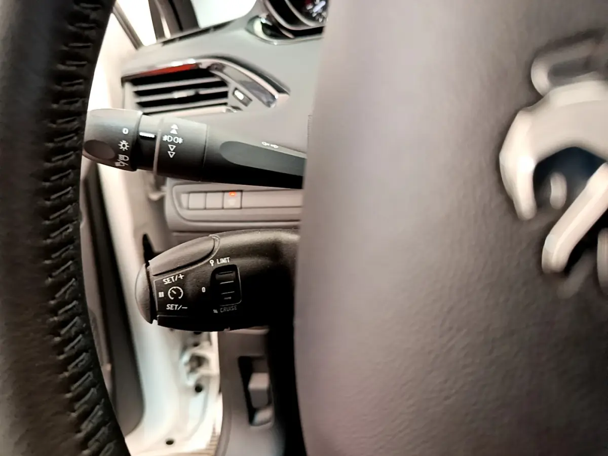 Gros plan sur le volant cuir et les commandes de régulateur de vitesse à gauche dans l’habitacle d’une Peugeot 208 blanche.