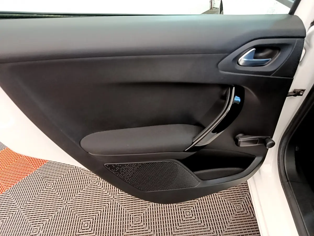 Porte intérieure côté gauche de la Peugeot 208 blanche, avec poignée noire brillante et manivelle de vitre manuelle.