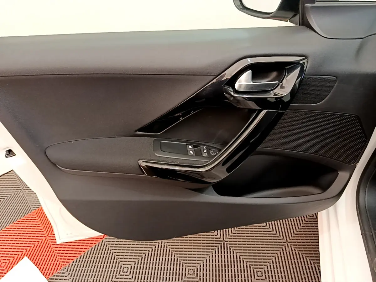 Intérieur de la porte avant gauche noire de la Peugeot 208 Puretech 82 Signature blanche, avec poignée et commandes électriques.