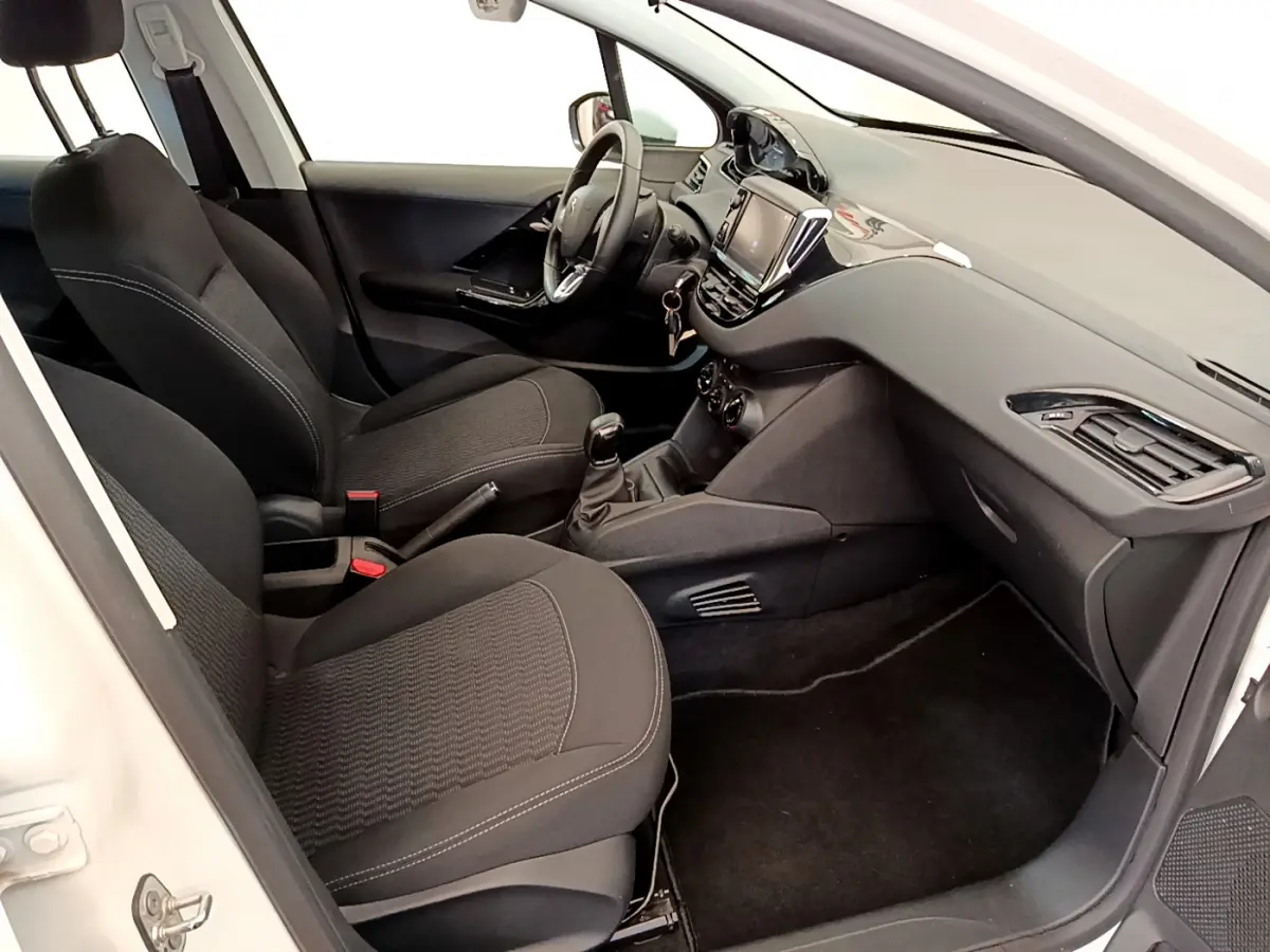 Intérieur de la Peugeot 208 blanc vue côté passager, sièges noirs et tableau de bord avec écran tactile.