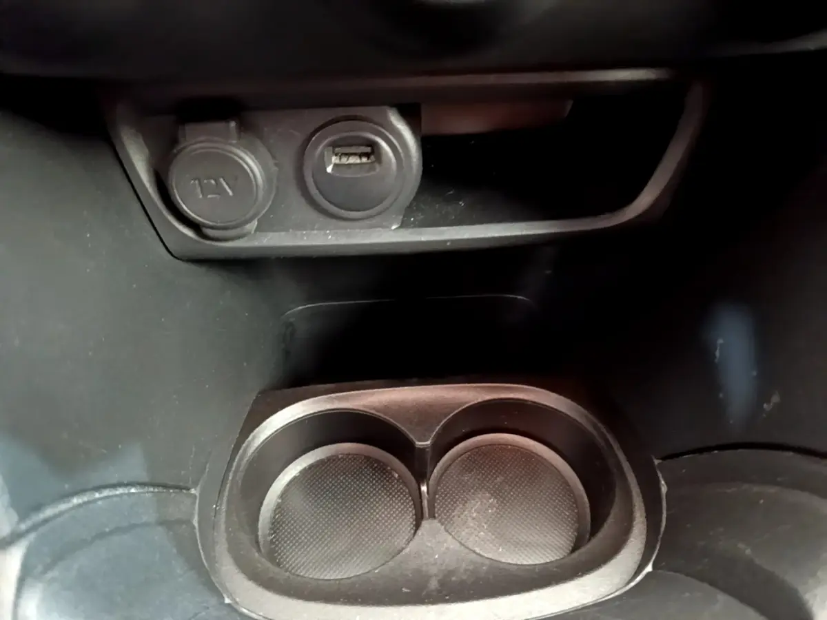 Gros plan sur la prise 12V et port USB au-dessus des porte-gobelets dans l’habitacle noir de la Peugeot 208 blanche