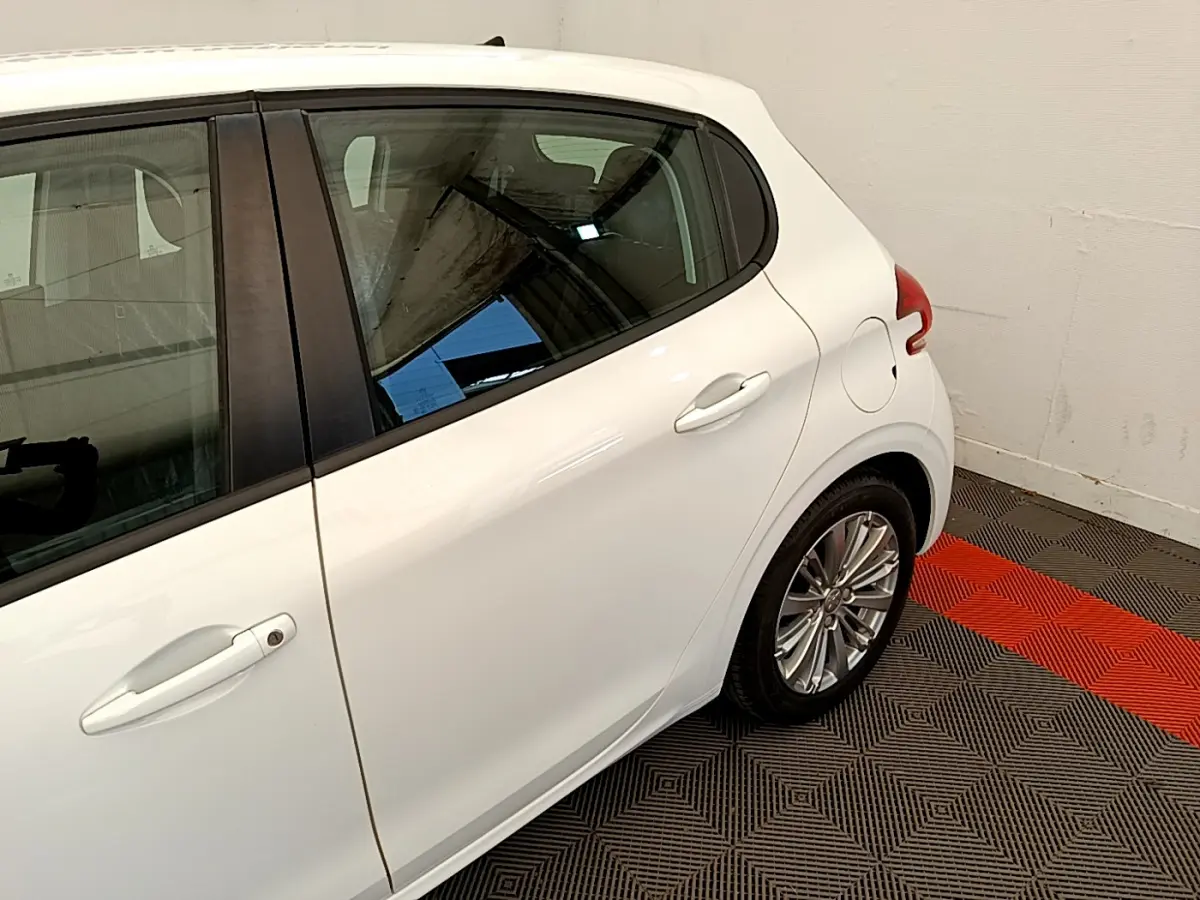 Vue côté droit arrière d'une Peugeot 208 Puretech 82 Signature blanche avec jante alliage et poignée de porte visible.