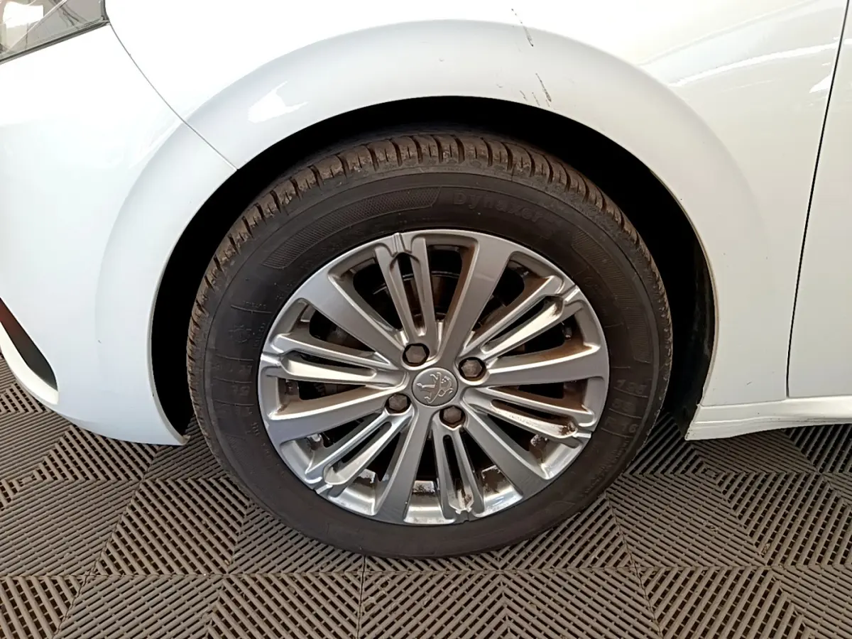 Gros plan sur la roue avant gauche de la Peugeot 208 blanche, mettant en valeur la jante alliage au design moderne.