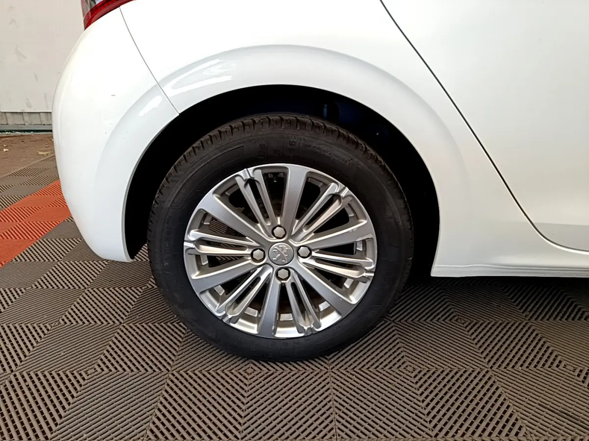 Gros plan sur la roue arrière droite d'une Peugeot 208 blanche, mettant en valeur la jante alliage au design moderne.