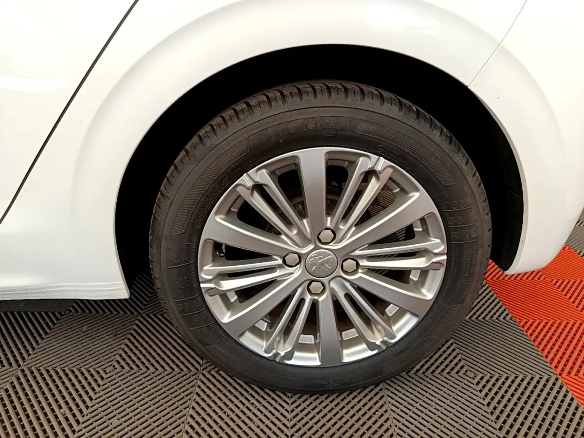 Gros plan sur la roue arrière droite d'une Peugeot 208 blanche avec jante alliage multibranches élégante.