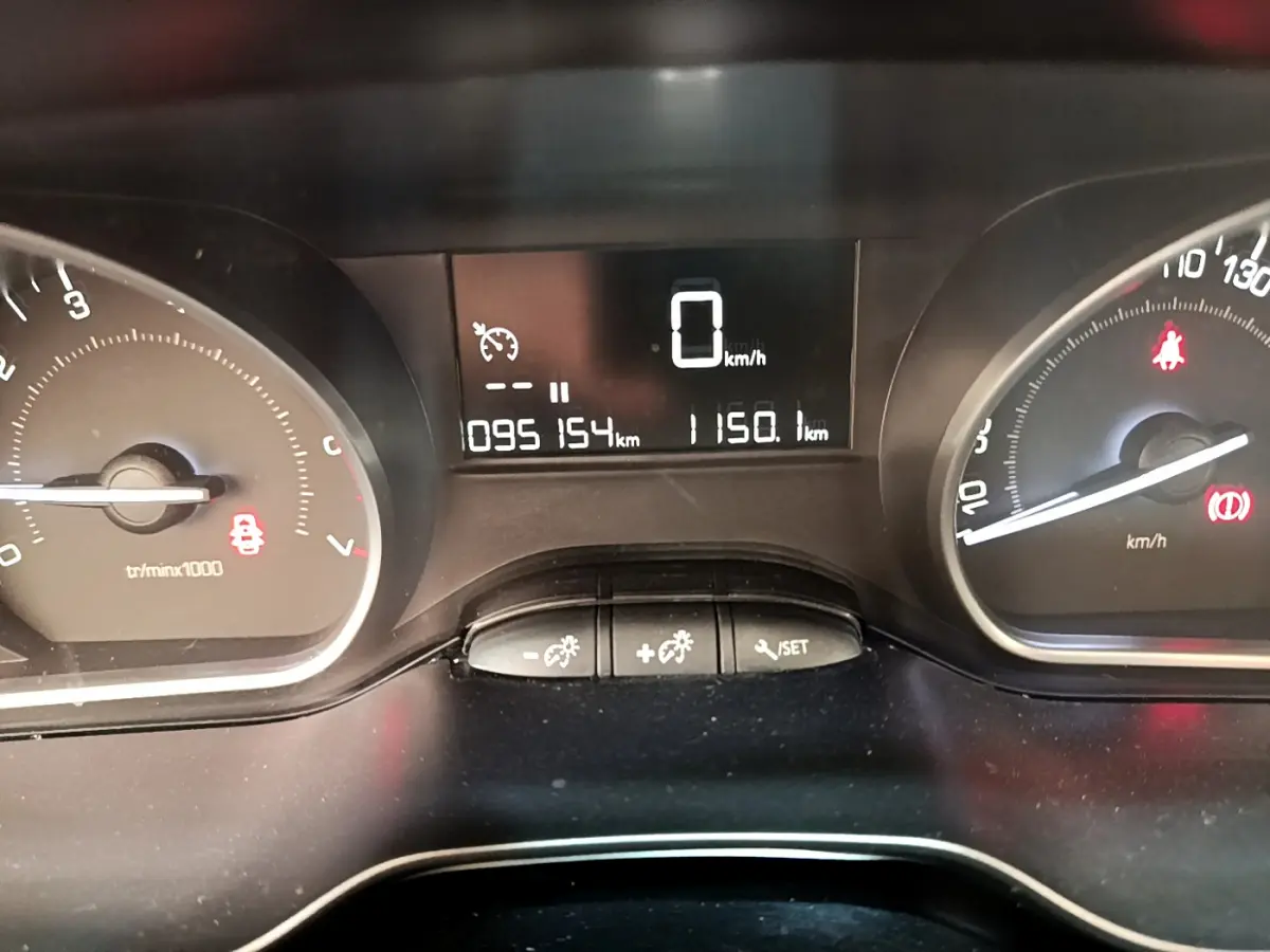 Tableau de bord de Peugeot 208 blanc, affichage numérique au centre avec compteur et témoins lumineux visibles.