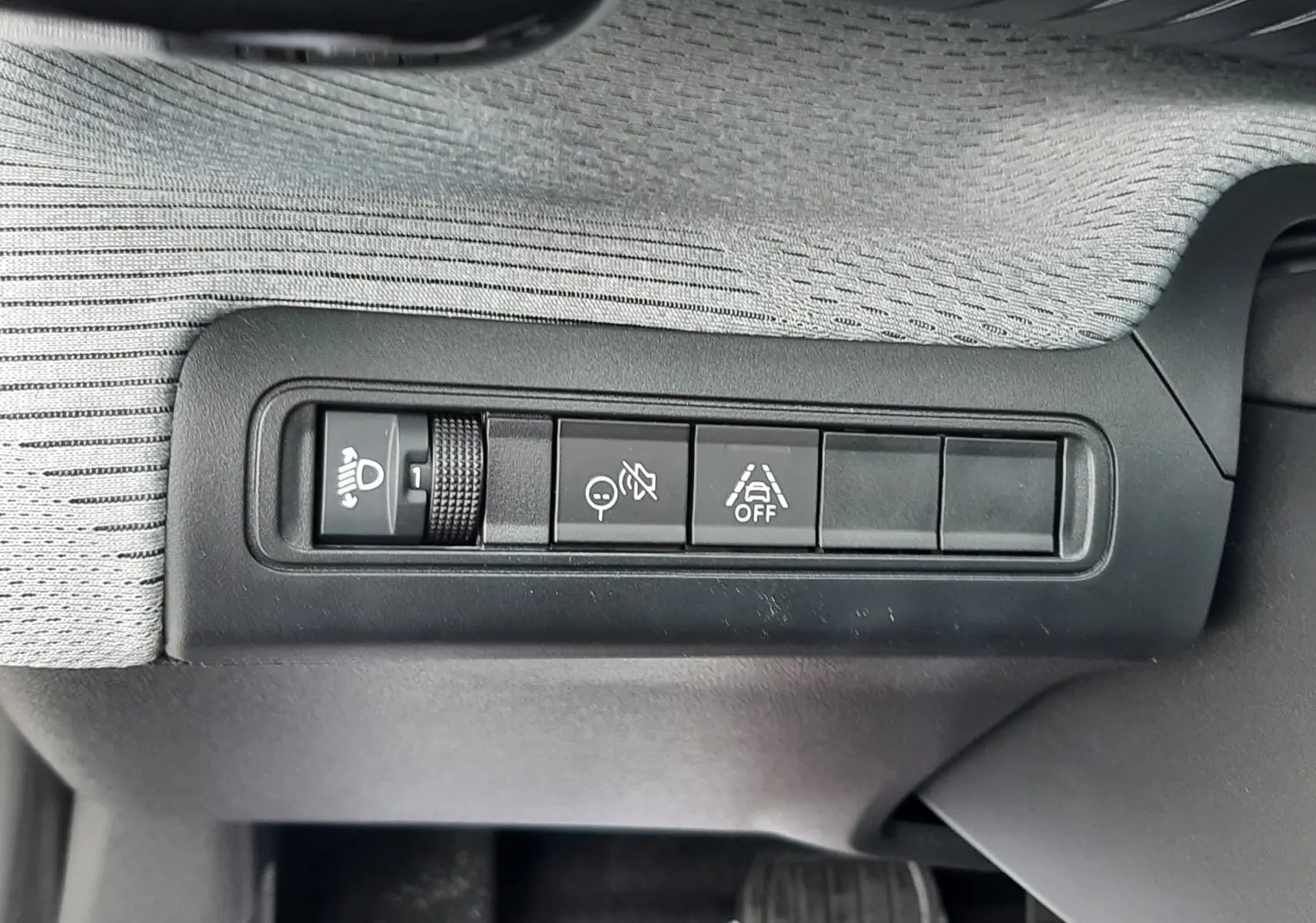 Gros plan sur les commandes de réglage des phares et d’aide à la conduite sur la planche de bord grise du Citroën C3 Aircross hybride 2025.