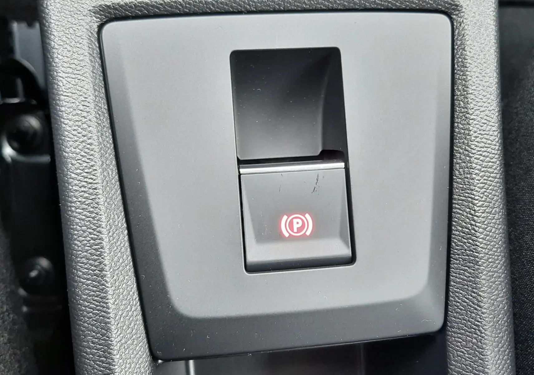 Gros plan sur le bouton de frein à main électronique rouge dans la console centrale d'une Citroën C3 Aircross hybride gris toit noir.