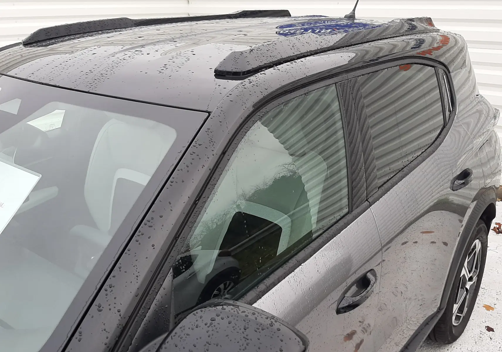 Vue 3/4 avant droit du Citroën C3 Aircross gris avec toit noir brillant et barres de toit noires sous la pluie.