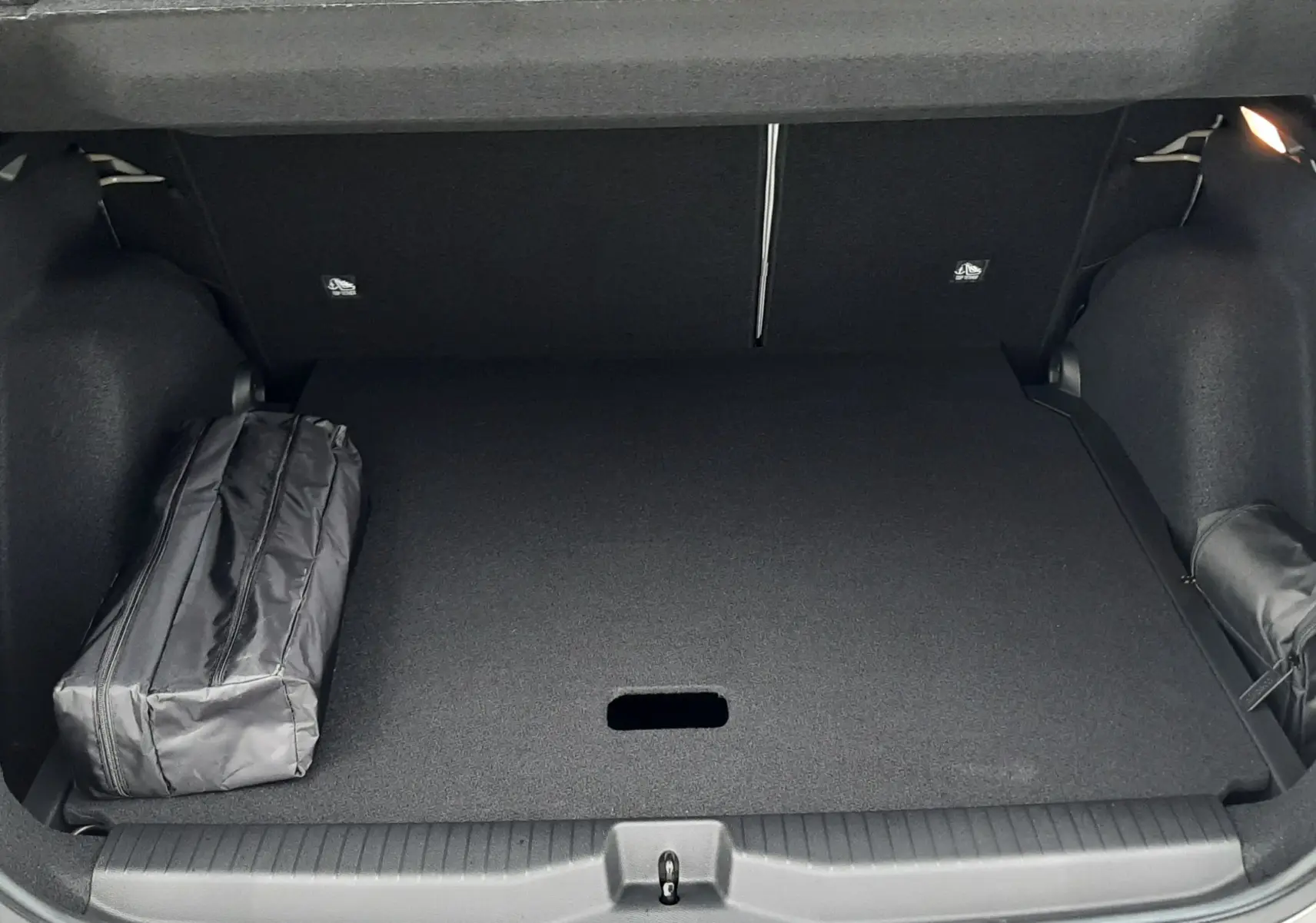 Coffre ouvert vu de l'arrière d'une Citroën C3 Aircross hybride gris avec toit noir, montrant un intérieur de coffre spacieux et un sac noir.