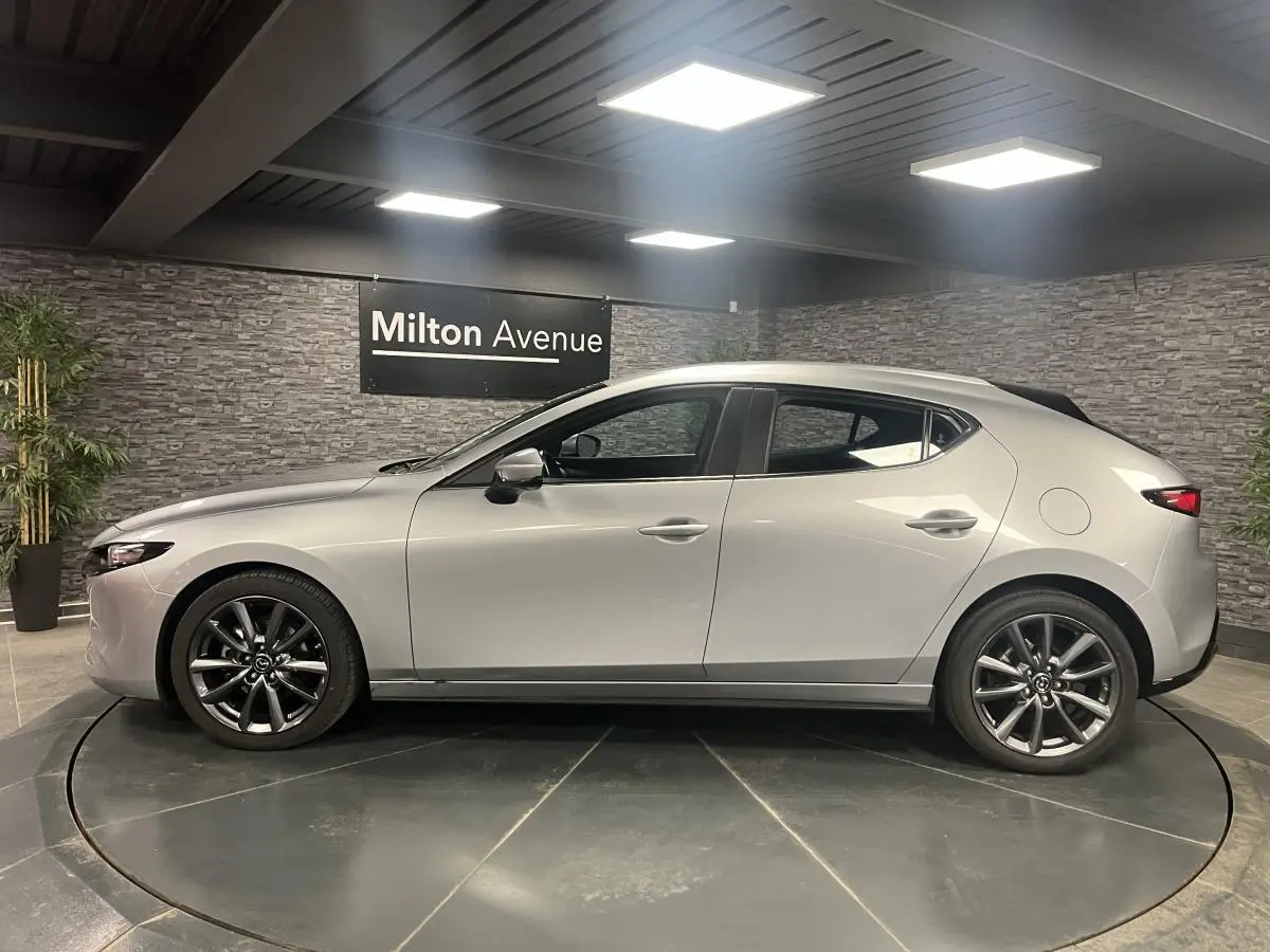 Profil côté gauche d'une Mazda3 gris métallisé 2023 avec jantes alliage 18 pouces dans un showroom.