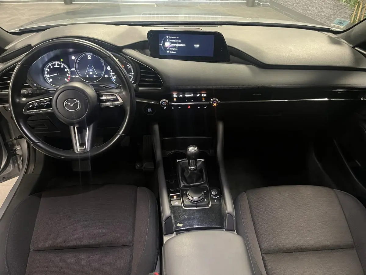 Intérieur de la Mazda3 2023 vu de face, tableau de bord noir avec écran central et volant cuir multifonctions.