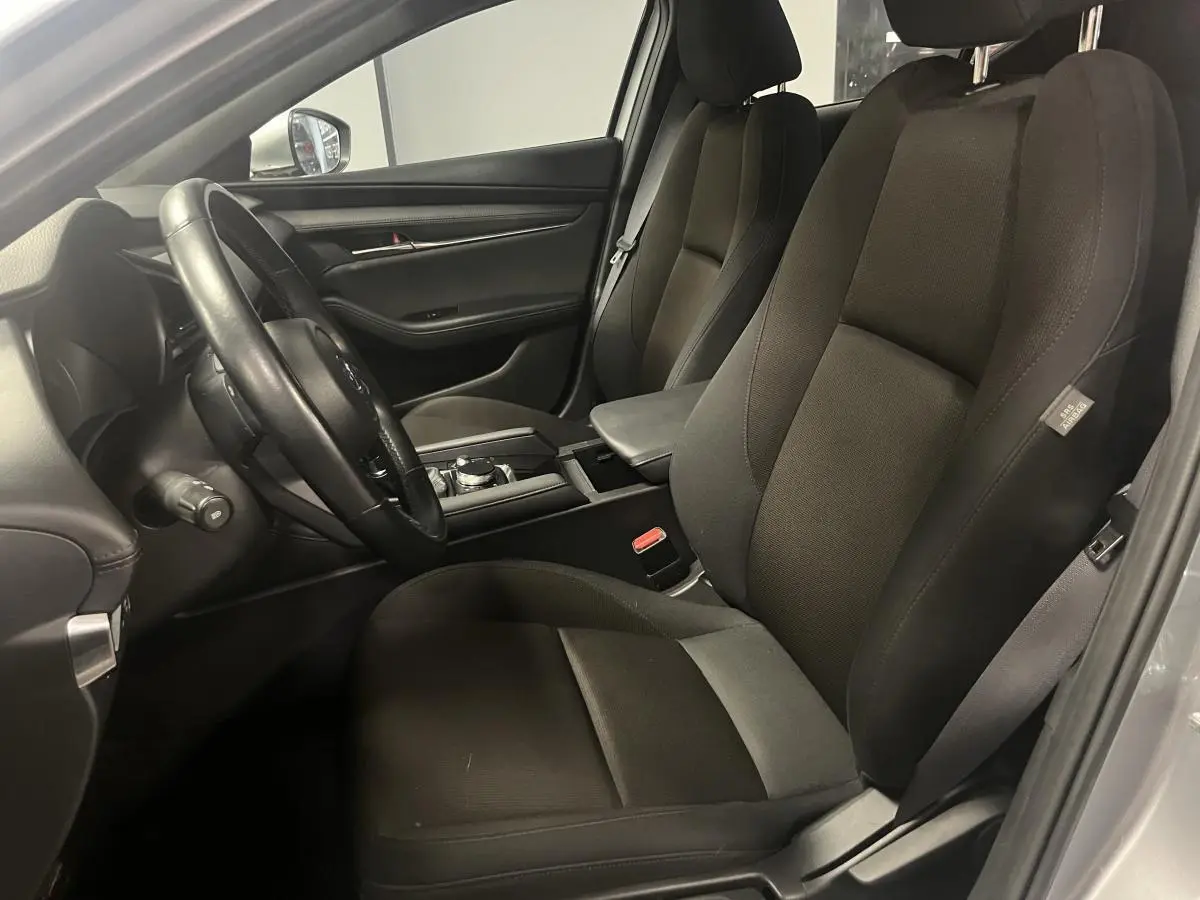 Intérieur noir de la Mazda3 2023, vue côté conducteur avec sièges tissu et console centrale visible.