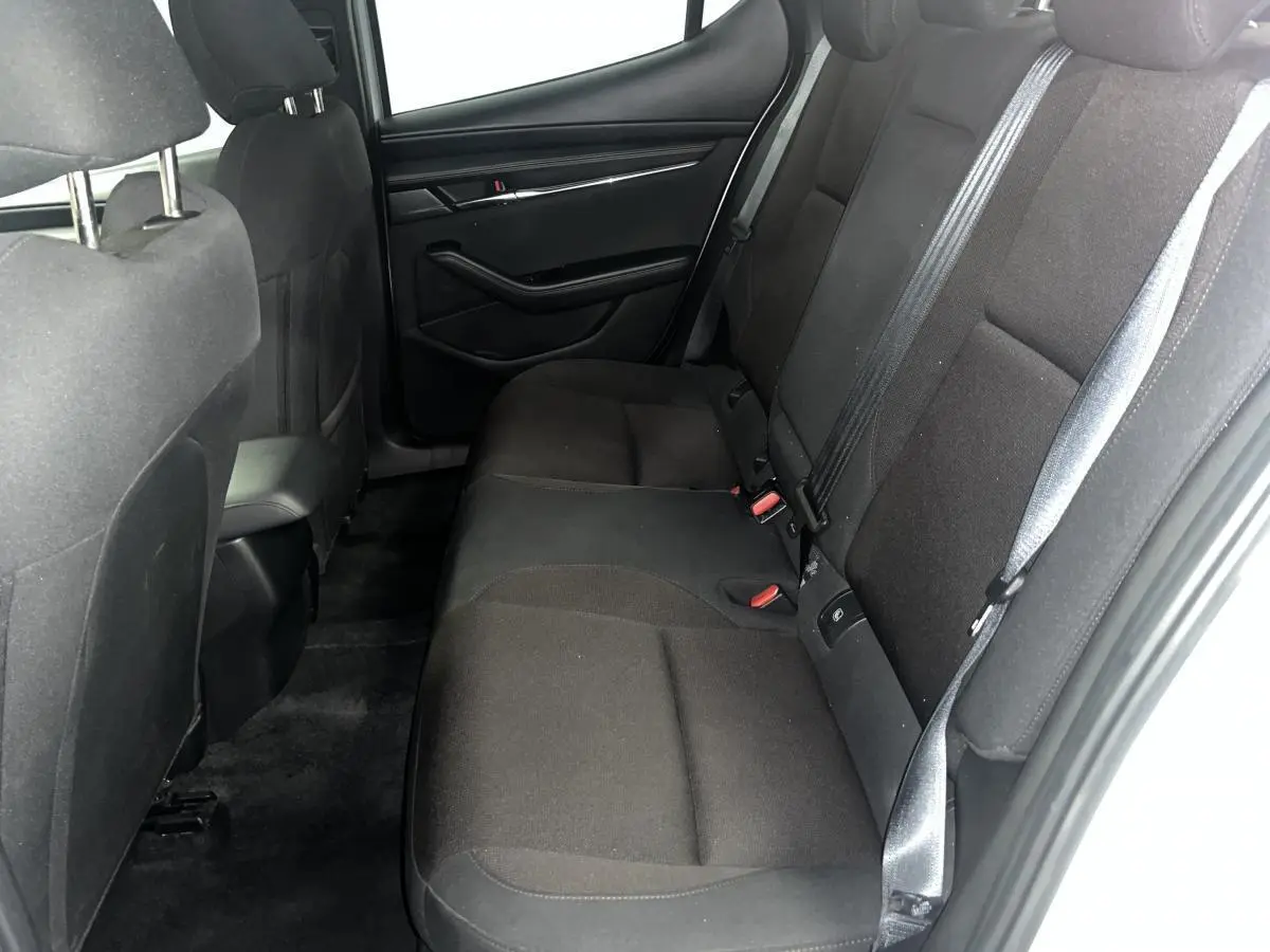 Vue latérale droite de l'intérieur arrière de la Mazda3 2023 avec sièges tissu noir et ceintures de sécurité grises.