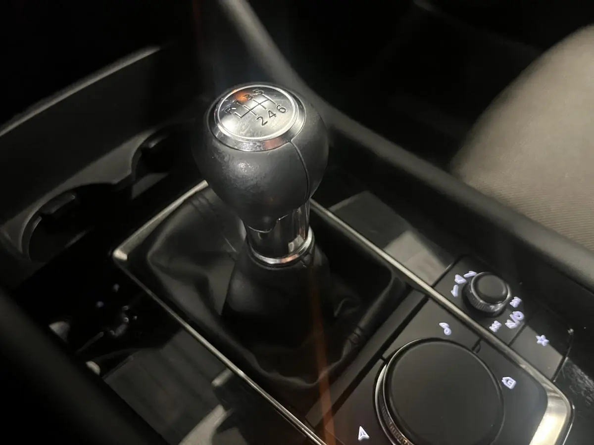Gros plan sur le levier de vitesses manuel noir de la Mazda3 2023, entouré de commandes et porte-gobelets.