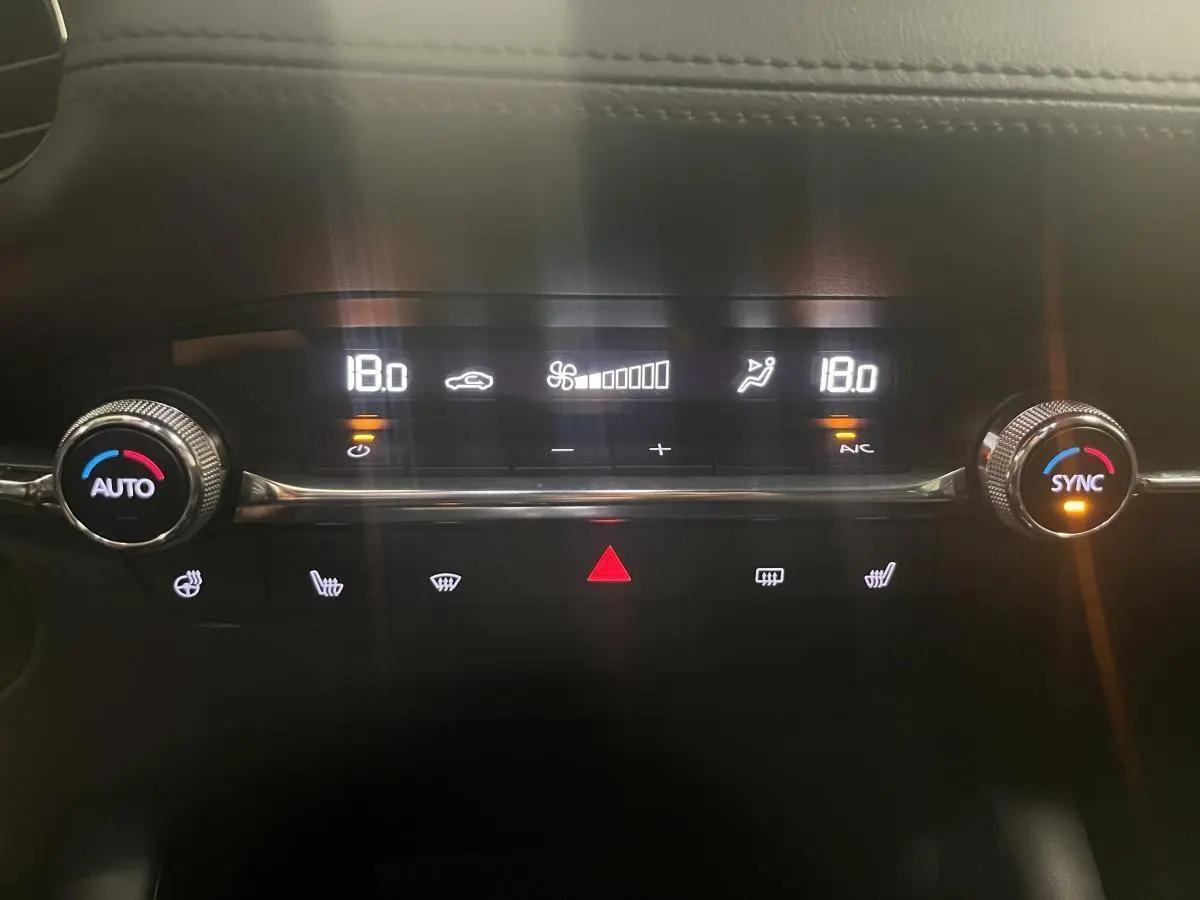 Gros plan sur la console centrale du Mazda3 gris 2023, affichant la climatisation automatique réglée à 18°C.