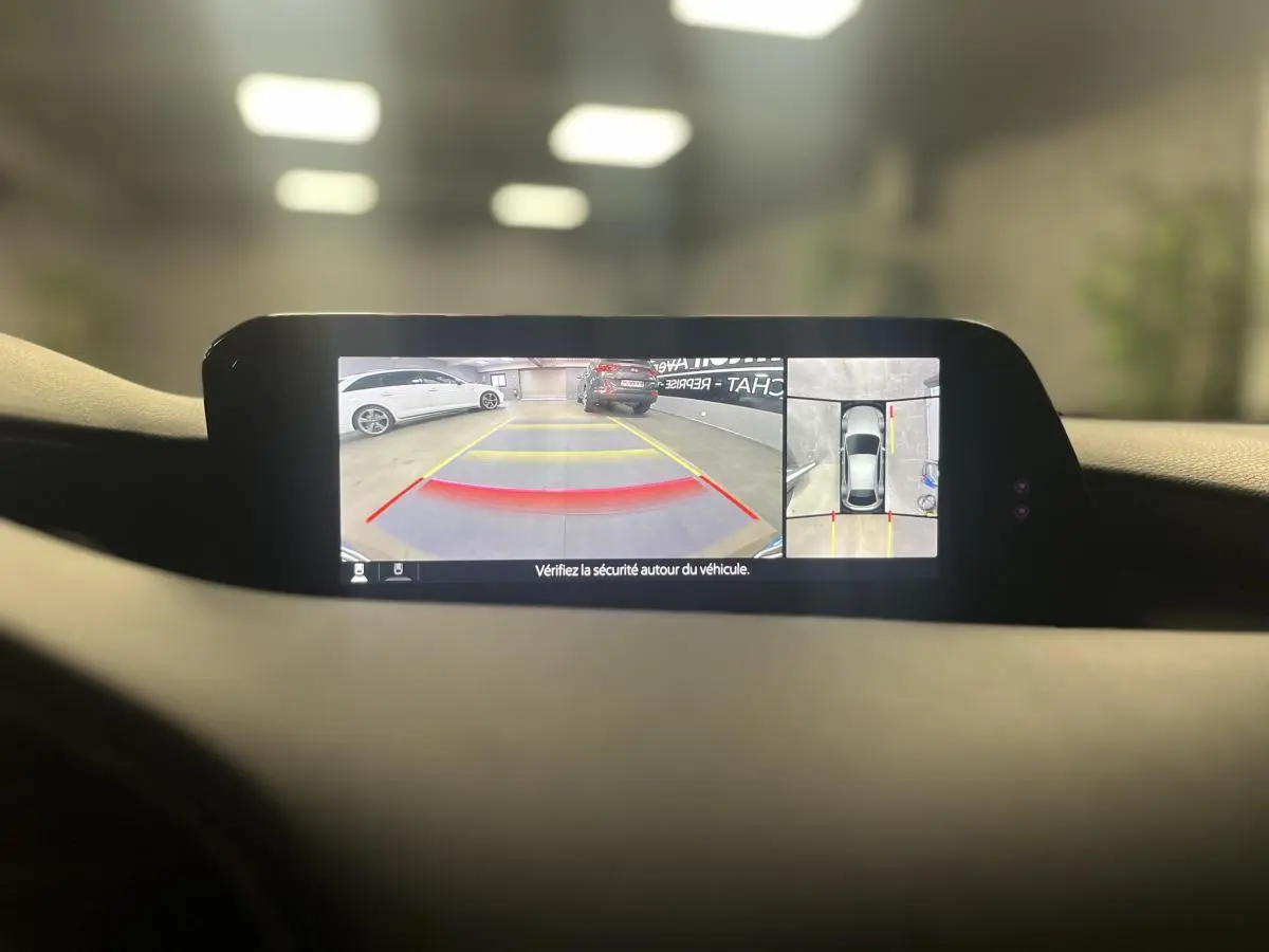 Affichage caméra 360° sur écran intérieur de Mazda3 grise, vue arrière et vue aérienne du stationnement.