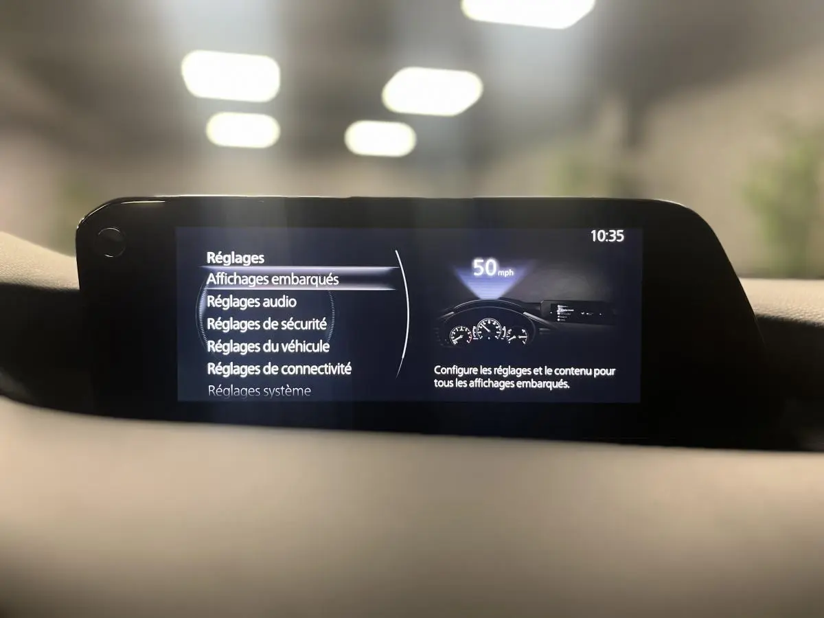 Écran central de la Mazda3 2023 affichant le menu des réglages embarqués dans un intérieur gris sobre.