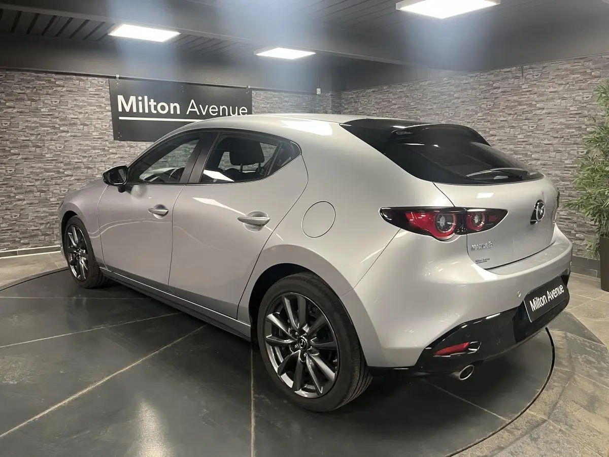 Vue 3/4 arrière droite d'une Mazda3 gris métallisé avec jantes alliage 18'' et becquet de toit noir.