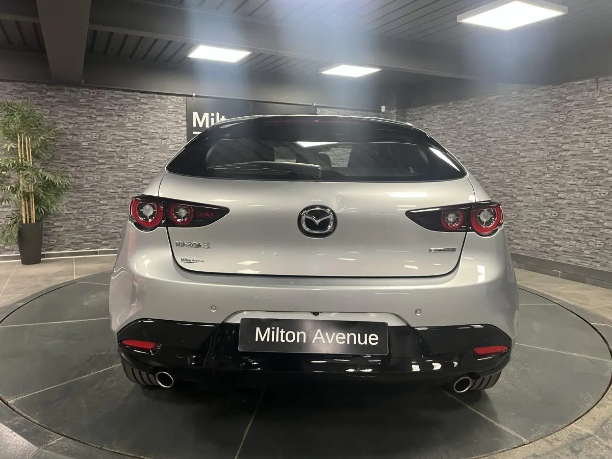 Vue arrière d'une Mazda3 gris métallisé avec double sortie d'échappement et toit noir dans un showroom.