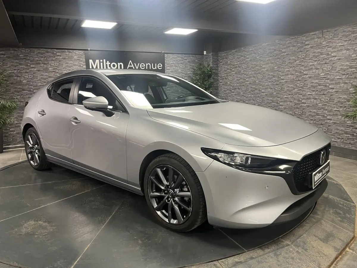 Vue 3/4 avant droite d'une Mazda3 gris métallisé avec calandre noire et jantes alliage 18 pouces grises.