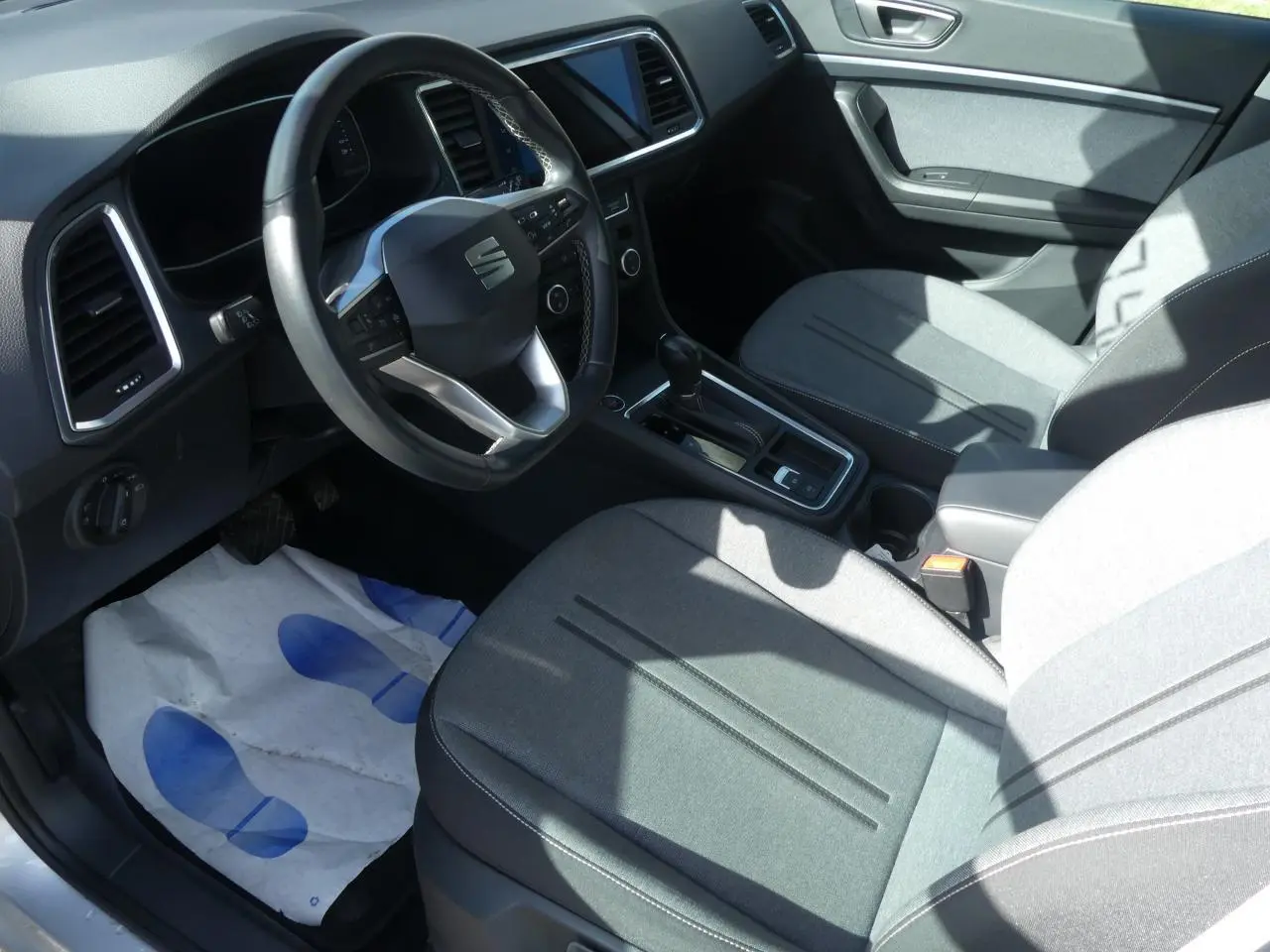 Intérieur avant droit d'un SEAT Ateca gris clair, volant cuir multifonctions et sellerie textile grise visible.